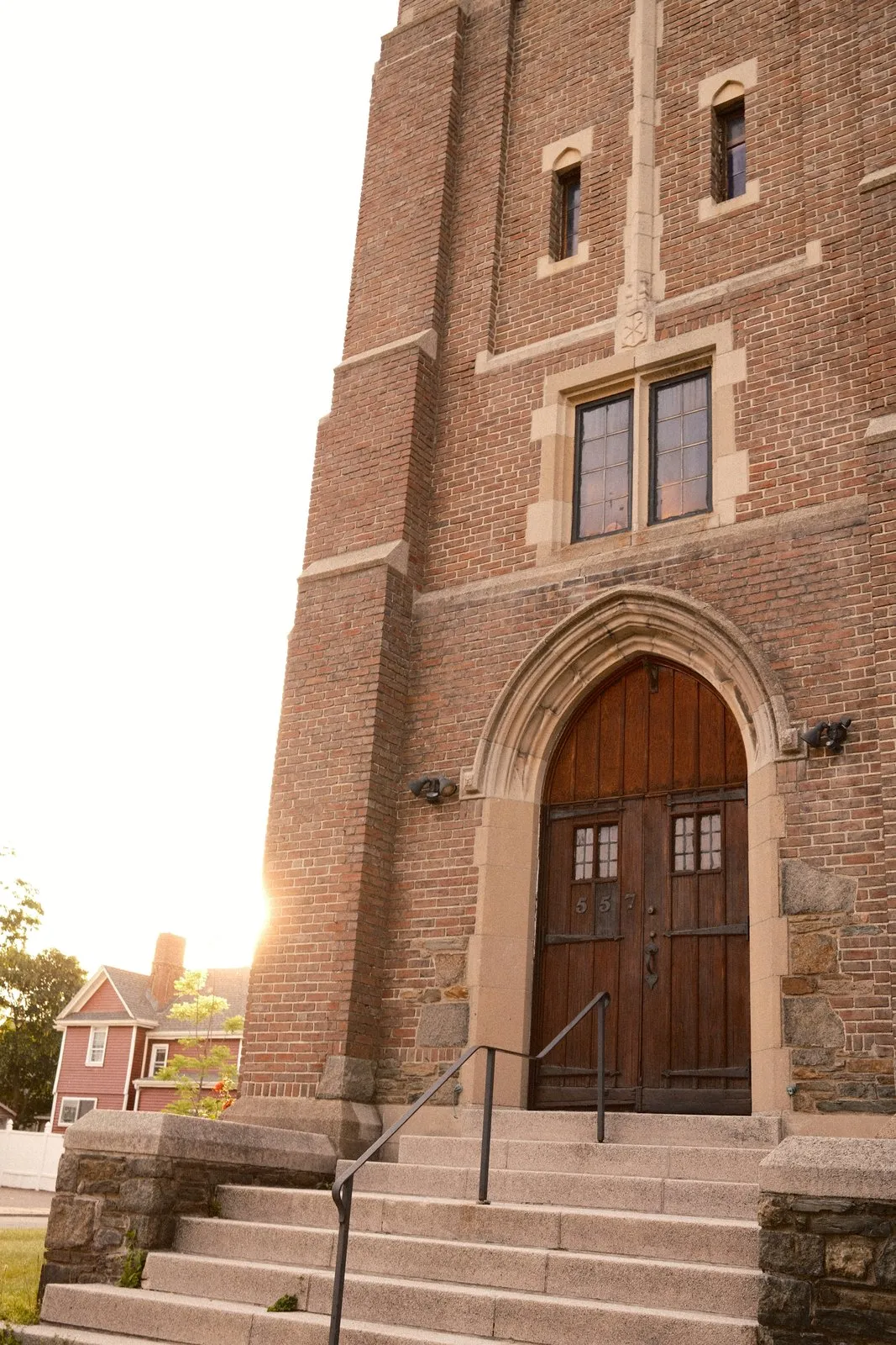 Paired wooden doors under a pointed stone arch at the top of granite steps, set in a brick tower