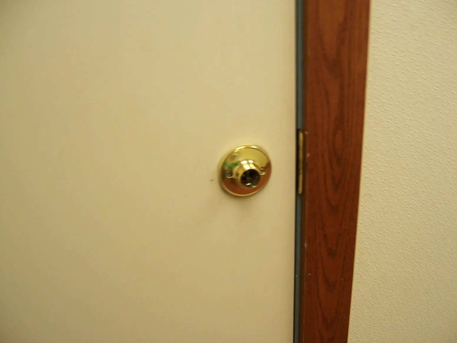 Close-up of a cream painted door where the brass knob is missing, leaving only the rose and spindle, beside a stained wood frame