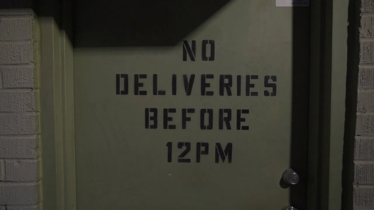 A green door with NO DELIVERIES BEFORE 12PM stencilled on it