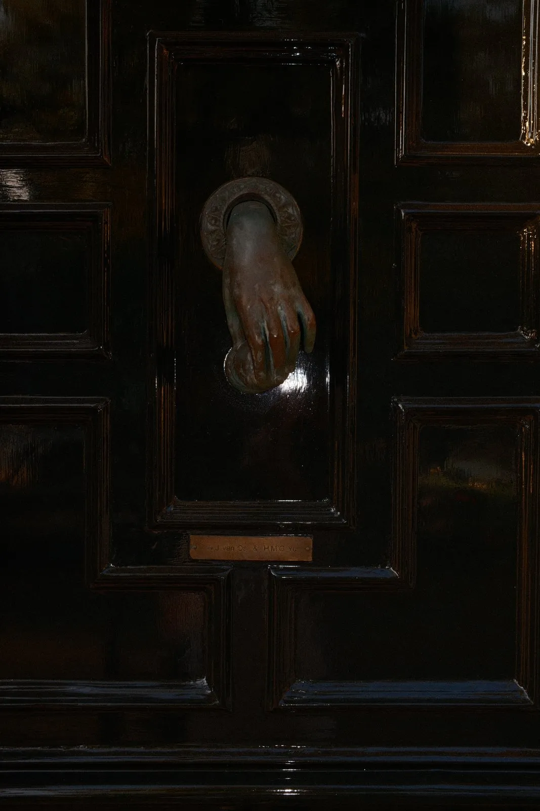 A bronze hand-shaped door knocker on a black lacquered raised-panel door