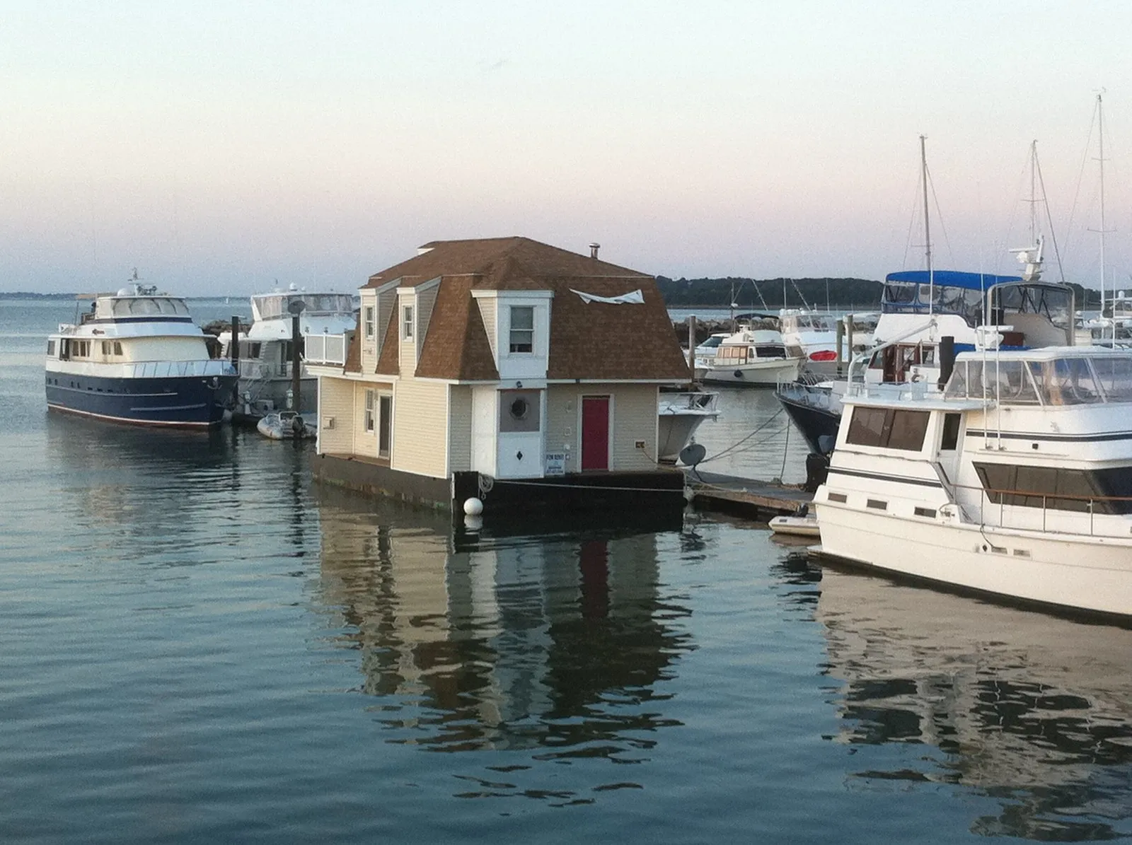 A houseboat with a red door moored in a marina among motor yachts