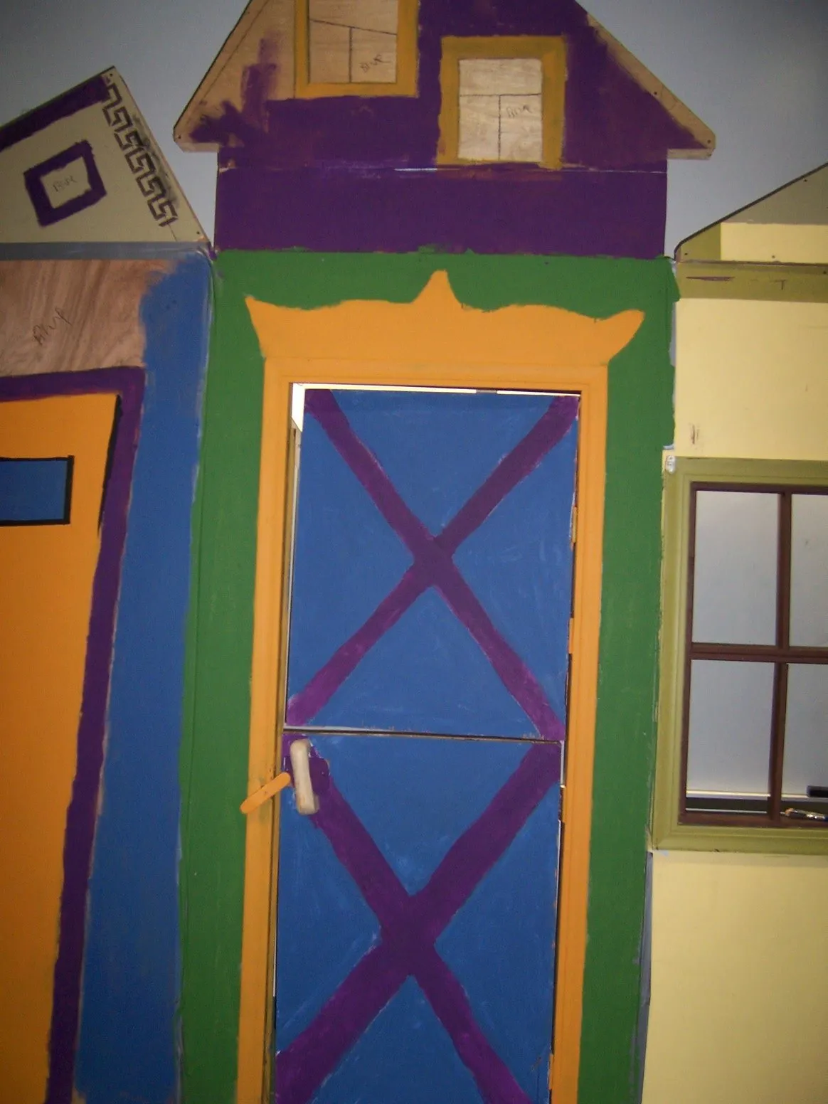 A painted mural of a colourful house with a blue door crossed by a purple X brace